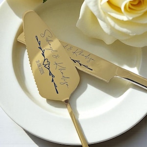 Può includere: Set di coltello e paletta per torta color oro su un piatto bianco. Il server è inciso con i nomi "Suhayl & Khadija" e la data "31.08.2025" in una scrittura decorativa, insieme a un motivo floreale. Anche il coltello ha i nomi incisi.