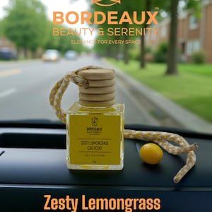 May include: A clear glass car air freshener with a wooden cap and a yellow label that reads "Zesty Lemongrass Car Scent." The image also includes a small yellow fruit and the text "Zesty Lemongrass."