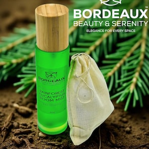 May include: A green Rainforest Eucalyptus room mist bottle with a wooden cap and a small beige drawstring bag. The bottle has a label with the text "Bordeaux Beauty & Serenity" and "Rainforest Eucalyptus Room Mist". The background includes greenery and the words "Rainforest Eucalyptus".