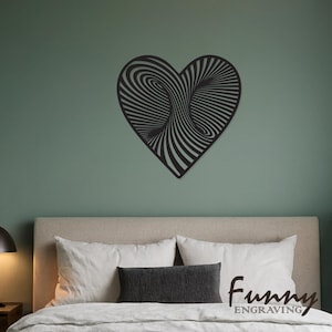 May include: A black heart-shaped wall art piece with a swirling, optical illusion design. The artwork is mounted on a muted green wall above a bed with white pillows and a gray pillow. The text "Funny Engraving" is visible.
