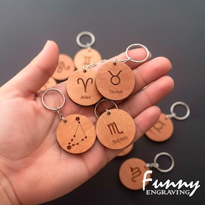 May include: Wooden round keychains with engraved zodiac symbols and names. The keychains are attached to silver keyrings. The image includes keychains for Aries, Taurus, and Scorpio. The text "Funny Engraving" is in the bottom right corner.