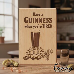 May include: Wooden sign with the text "Have a Guinness when you're TIRED". The sign features an engraved image of a pint of Guinness atop a turtle. The sign is made of light-coloured wood.