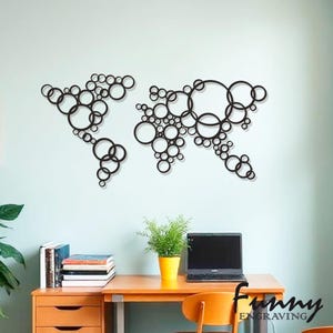 Könnte beinhalten: Schwarze Wandkunst, die eine Weltkarte aus miteinander verbundenen Kreisen darstellt. Das Kunstwerk ist an einer hellblauen Wand angebracht. Im Vordergrund befindet sich ein Schreibtisch mit Laptop, Pflanze und Büchern.