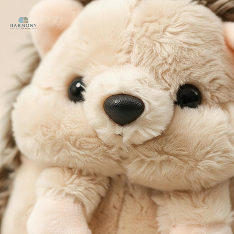 May include: A close-up shot of a soft, plush hedgehog toy. The toy has beige fur and darker brown spines. It has large, black eyes and a black nose. The toy is designed to be cuddly and is suitable for children.