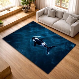Puede incluir: Una alfombra rectangular con una imagen realista de una orca nadando en agua azul oscuro. El diseño de la alfombra incluye las distintivas marcas blancas y negras de la orca, creando un contraste llamativo con la textura del agua. La alfombra está colocada sobre un suelo de madera.