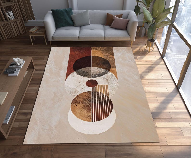 May include: A rectangular area rug with a geometric design in shades of beige, brown, and rust. The rug features abstract shapes including circles, ovals, and vertical lines. The rug is placed on a hardwood floor, with a sofa and plants in the background.