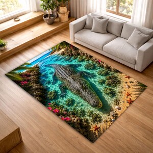 Op de afbeelding: Een rechthoekig vloerkleed met een gedetailleerde afbeelding van een alligator in een tropische lagune. Het kleed heeft een turquoise waterachtergrond met zand, zeesterren en weelderig groen. De alligator is grijs en bruin.