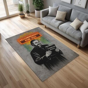 K&ouml;nnte beinhalten: Rechteckiger Teppich mit grauem Hintergrund. Er zeigt eine Schwarz-Wei&szlig;-Illustration eines Mannes, der ein Buch mit dem Titel "ALGORITHM MANUAL" h&auml;lt. &Uuml;ber dem Mann befindet sich ein Leuchtschild mit der Aufschrift "RECOMMENDED FOR YOU".