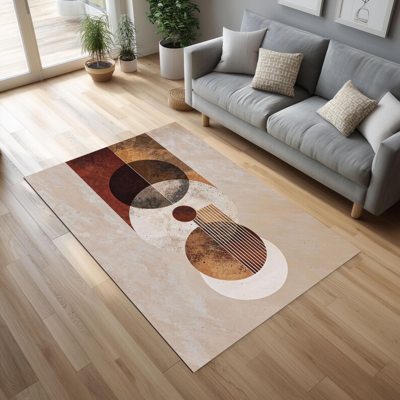 May include: A rectangular area rug with an abstract geometric design. The rug features a beige background with brown, rust, and white circular and semi-circular shapes. The rug is placed on a hardwood floor in a living room setting.