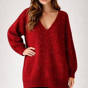 Può includere: Un maglione rosso a maniche lunghe con scollo a V profondo. Il maglione ha una maglia strutturata con macchie di colore. Le maniche sono lunghe e la vestibilità è ampia. La modella indossa pantaloni neri.