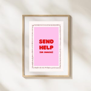 May include: Framed art print with a pink background and the words "SEND HELP (OR SNACKS)" in red. The print is surrounded by a white border with a dotted design and is set in a light brown wooden frame.