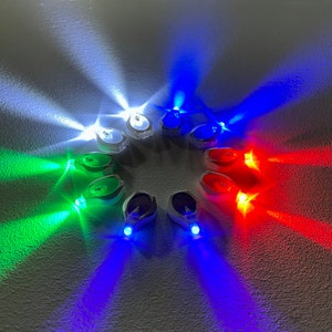 Op de afbeelding: Een cirkelvormige opstelling van kleine, veelkleurige LED-lampjes. De lampjes zijn wit, blauw, groen en rood en werpen kleurrijke stralen. Elke lamp heeft een transparante plastic behuizing.