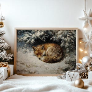 Può includere: Una stampa incorniciata raffigura una volpe addormentata nella neve, rannicchiata sotto rami di abete innevati. La volpe ha una pelliccia marrone-rossiccia ed è raggomitolata nella neve. L'opera d'arte è in una cornice di legno, con decorazioni natalizie sullo sfondo.