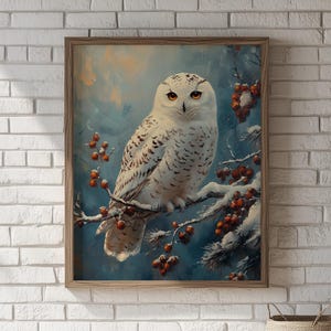 May include: A framed print of a snowy owl perched on a snow-covered branch with red berries. The owl has white feathers with dark spots and bright orange eyes. The background is a soft blue and the frame is a light brown.