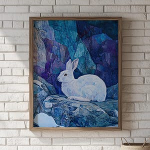 Puede incluir: Impresión artística enmarcada que presenta un conejo blanco sobre una formación rocosa. El fondo muestra un paisaje montañoso azul y púrpura. La obra de arte está encerrada en un marco de madera, creando una estética inspirada en la naturaleza.