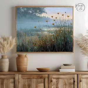 May include: A framed landscape print depicts a misty marsh scene with tall grasses and yellow wildflowers. The artwork has a soft, muted color palette with a wooden frame. The print is displayed on a wooden cabinet with decorative vases and a bowl.