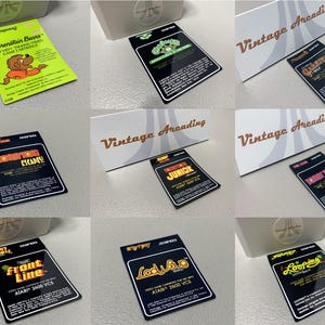 May include: A collection of vintage Atari 2600 video game cartridges. The cartridges feature colorful labels with game titles like "Front Line," "Looping," and "Berenstain Bears." The phrase "Vintage Arcading" is printed on a white display.