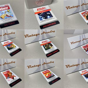 May include: A collection of Atari video game cartridges, each with colorful game art and black labels. The games include Asterix, Asteroids, Battlezone, Centipede, Crazy Climber, Crystal Castles, Dig Dug, and ET. The cartridges are displayed with a "Vintage Arcading" logo.