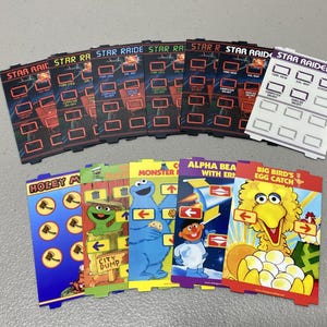 May include: A collection of rectangular plastic game overlays for a console. The top row features six Star Raiders overlays with black backgrounds and red or white grid buttons. The bottom row displays five colorful Sesame Street themed overlays.