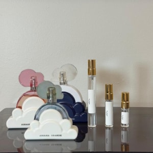 Può includere: Una collezione di bottiglie di profumo Ariana Grande di varie dimensioni. Le bottiglie hanno la forma di nuvole e sono disponibili in rosa, blu e bianco. Sono presenti anche diversi flaconi spray più piccoli, da viaggio, con tappi dorati.