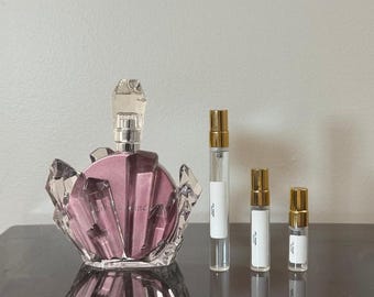 以下が含まれることがあります： 香水瓶と3つの小さなサンプルバイアル。香水瓶は、クリスタルのようなキャップとベースが付いた、明るいピンク色です。サンプルバイアルには、金色のキャップと白いラベルが付いています。