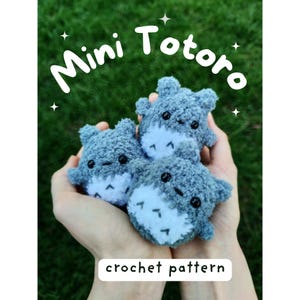 May include: Three mini crochet Totoro figures in shades of gray and white are displayed. The figures have black eyes and a white belly with three black markings. The text "Mini Totoro" and "crochet pattern" are written in white.