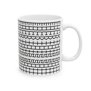 May include: White ceramic mug with a black geometric pattern wrapping around the exterior. The pattern consists of various shapes and lines, creating a textured appearance. The mug has a curved handle and is suitable for hot or cold beverages.