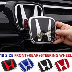May include: A black and chrome Honda emblem badge for a vehicle front, rear, or steering wheel. The emblem features a reflective H logo on a glossy black background. Below, four additional emblem variations are shown in red, blue, black, and white.