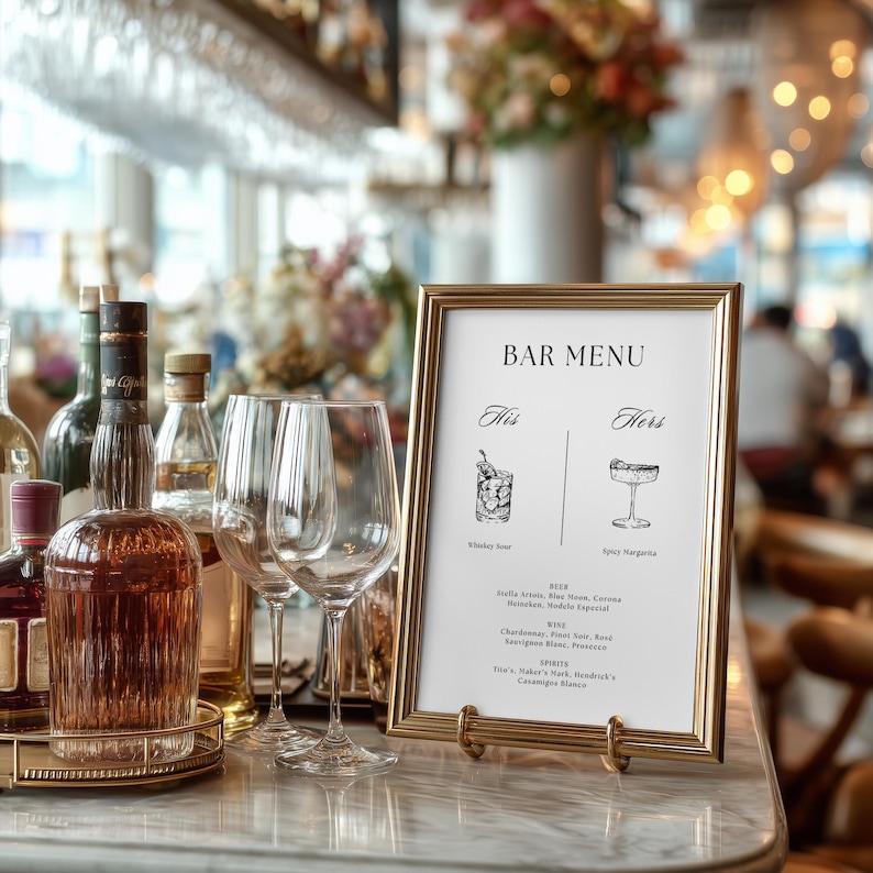 Puede incluir: Un men&uacute; de bar con marco dorado con el texto "Bar Menu" en la parte superior. El men&uacute; presenta ilustraciones de c&oacute;cteles y una lista de bebidas. Copas de vino y botellas de licor est&aacute;n en el fondo, sobre una superficie de m&aacute;rmol.