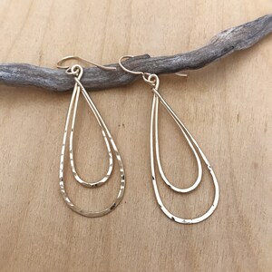 Peut inclure: Une paire de boucles d'oreilles dor&eacute;es en forme de goutte d'eau &agrave; deux niveaux. Les boucles d'oreilles ont une texture martel&eacute;e et sont suspendues &agrave; de simples crochets d'oreilles. Le design est minimaliste et &eacute;l&eacute;gant.
