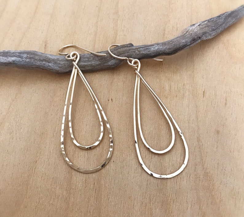 Peut inclure: Une paire de boucles d'oreilles dor&eacute;es en forme de goutte d'eau &agrave; deux niveaux. Les boucles d'oreilles ont une texture martel&eacute;e et sont suspendues &agrave; de simples crochets d'oreilles. Le design est minimaliste et &eacute;l&eacute;gant.