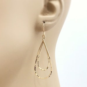 Peut inclure: Boucles d'oreilles dor&eacute;es en forme de double goutte d'eau. Les boucles d'oreilles ont une texture martel&eacute;e et sont suspendues &agrave; un simple crochet. Le design pr&eacute;sente deux formes de goutte d'eau imbriqu&eacute;es, cr&eacute;ant un effet superpos&eacute;. Accessoire de bijouterie.