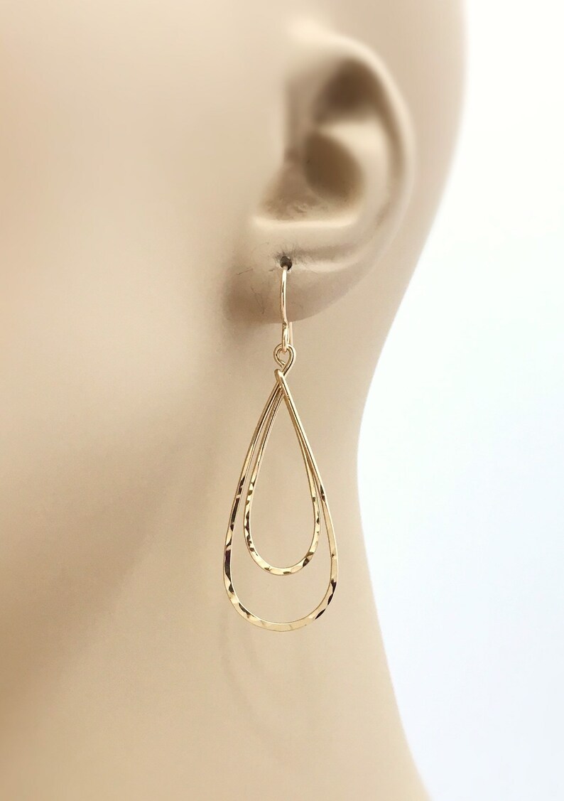 Peut inclure: Boucles d'oreilles dor&eacute;es en forme de double goutte d'eau. Les boucles d'oreilles ont une texture martel&eacute;e et sont suspendues &agrave; un simple crochet. Le design pr&eacute;sente deux formes de goutte d'eau imbriqu&eacute;es, cr&eacute;ant un effet superpos&eacute;. Accessoire de bijouterie.