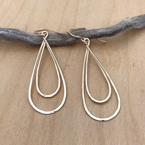 Peut inclure: Une paire de boucles d'oreilles dor&eacute;es en forme de goutte d'eau. Chaque boucle d'oreille pr&eacute;sente un double design en forme de goutte d'eau, avec une forme de goutte d'eau nich&eacute;e &agrave; l'int&eacute;rieur de l'autre. Les boucles d'oreilles sont suspendues &agrave; un crochet simple.
