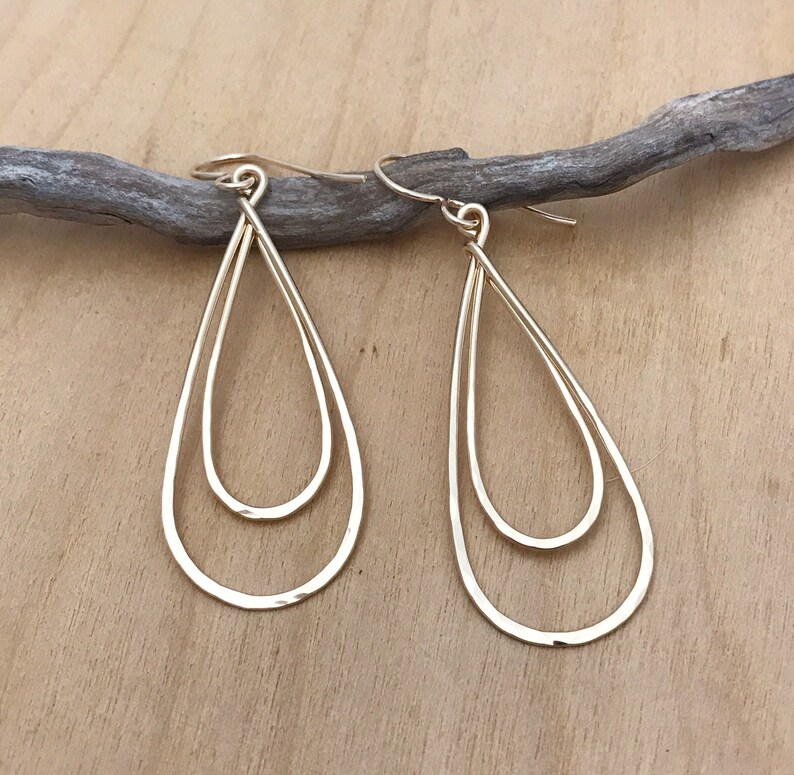 Peut inclure: Une paire de boucles d'oreilles dor&eacute;es en forme de goutte d'eau. Chaque boucle d'oreille pr&eacute;sente un double design en forme de goutte d'eau, avec une forme de goutte d'eau nich&eacute;e &agrave; l'int&eacute;rieur de l'autre. Les boucles d'oreilles sont suspendues &agrave; un crochet simple.