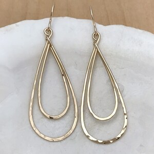 Peut inclure: Une paire de boucles d'oreilles dor&eacute;es en forme de goutte d'eau. Chaque boucle d'oreille pr&eacute;sente un double design en forme de goutte d'eau, avec une texture martel&eacute;e sur la goutte ext&eacute;rieure. Les boucles d'oreilles sont suspendues &agrave; un simple crochet.