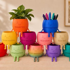 May include: A pyramid arrangement of ten colourful, round, smiling planters with dangling legs. Each planter features a unique engraved message including Thank You, Happy Birthday, You Are Amazing, Best Teacher, Best Mum, Best Dad, Best Friend, Congratulations, Happy Anniversary, New Home, and Thinking of You.
