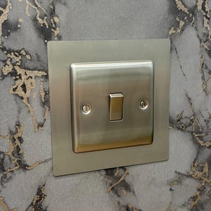May include: A brushed nickel light switch with a rectangular faceplate. The switch has a toggle and two small screws. The background is a gray and gold marble pattern.