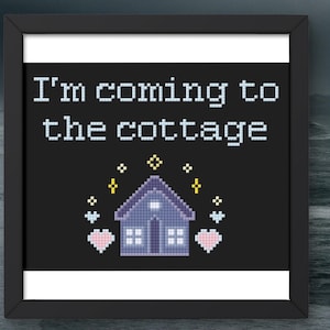 May include: Framed cross-stitch art with the text "I'm coming to the cottage" above a pixelated house with hearts and stars on a black background. The frame is black with a white border.