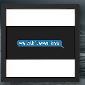 May include: Framed art print with a black frame, featuring a text message bubble that reads "we didn't even kiss" in pixelated blue text on a black background. The frame is set against a blurred ocean backdrop.