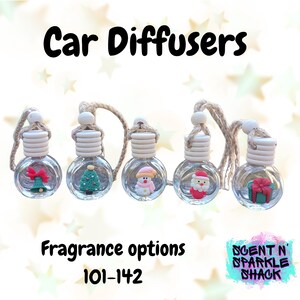May include: Five clear glass car diffusers with holiday-themed decorations, including a red bow, Christmas tree, snowman, Santa Claus, and a gift box. Each diffuser has a wooden top and a string for hanging. The text "Car Diffusers" and "Fragrance options 101-142" are displayed.