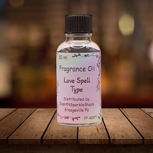 Puede incluir: Una botella de vidrio transparente de aceite de fragancia con una tapa negra. La etiqueta dice "Fragrance Oil Love Spell Type" e incluye el nombre y la direcci&oacute;n del distribuidor. La botella contiene 30 ml de aceite.