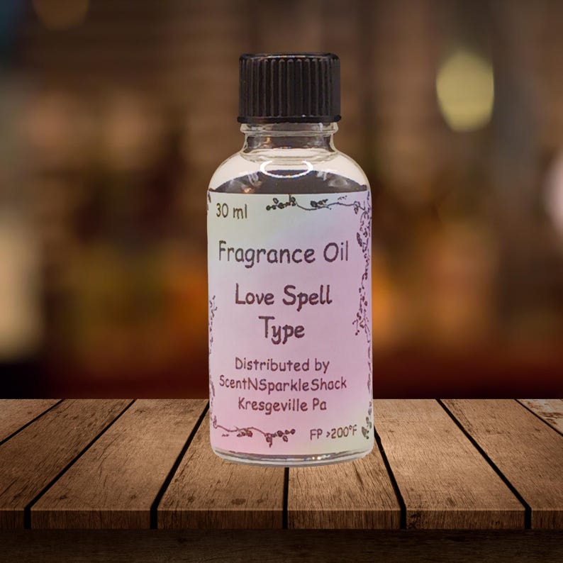 Puede incluir: Una botella de vidrio transparente de aceite de fragancia con una tapa negra. La etiqueta dice "Fragrance Oil Love Spell Type" e incluye el nombre y la direcci&oacute;n del distribuidor. La botella contiene 30 ml de aceite.
