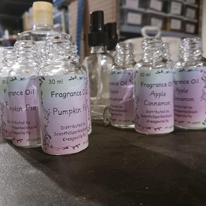 Puede incluir: Una colecci&oacute;n de botellas de aceite de fragancia de vidrio transparente con etiquetas. Las etiquetas muestran los nombres de las fragancias "Pumpkin Pie" y "Apple Cinnamon". Cada botella contiene 30 ml de aceite. Las botellas est&aacute;n dispuestas sobre una superficie.