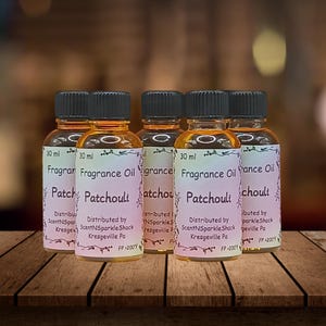 Puede incluir: Seis peque&ntilde;os frascos de vidrio de aceite de fragancia de pachul&iacute;, cada uno etiquetado "30 ml". Las etiquetas dicen "Fragrance Oil Patchouli" e incluyen informaci&oacute;n del distribuidor. Los frascos tienen tapas negras y aceite de color &aacute;mbar.