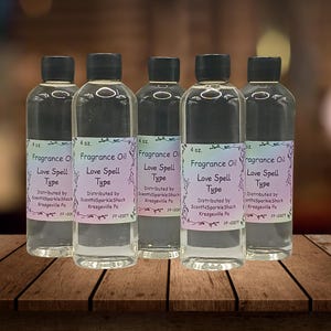 Puede incluir: Cinco botellas de vidrio transparente de aceite de fragancia con tapas negras. Cada botella tiene una etiqueta que dice "Fragrance Oil Love Spell Type". Las botellas son de 118 ml cada una y se muestran sobre una superficie de madera.
