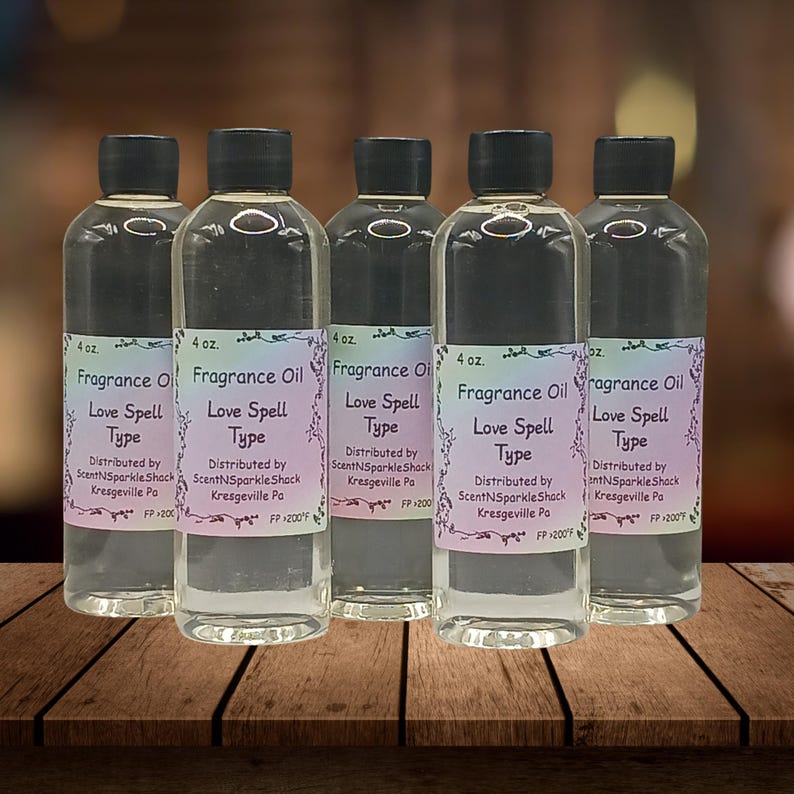 Puede incluir: Cinco botellas de vidrio transparente de aceite de fragancia con tapas negras. Cada botella tiene una etiqueta que dice "Fragrance Oil Love Spell Type". Las botellas son de 118 ml cada una y se muestran sobre una superficie de madera.