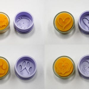 Könnte beinhalten: Eine Sammlung von vier Kerzenformen-Paaren. Jedes Paar besteht aus einer gelben Kerze in einem Glasbehälter und einer lila Form. Die Designs umfassen einen Marienkäfer, ein Herz, einen Pfotenabdruck und ein Herzdesign.