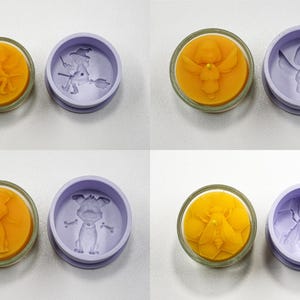 May include: A collection of four pairs of round, decorative molds. Each pair features a yellow wax candle with a detailed design and a matching purple mold. Designs include a witch, angel, dog, and bee.