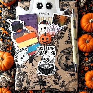 May include: A Halloween-themed gift set featuring a ghost-shaped container with the text "SPALIFE". The set includes stickers, a pen, and a decorative pumpkin. The background is decorated with pumpkins, spiderwebs, and spiders.